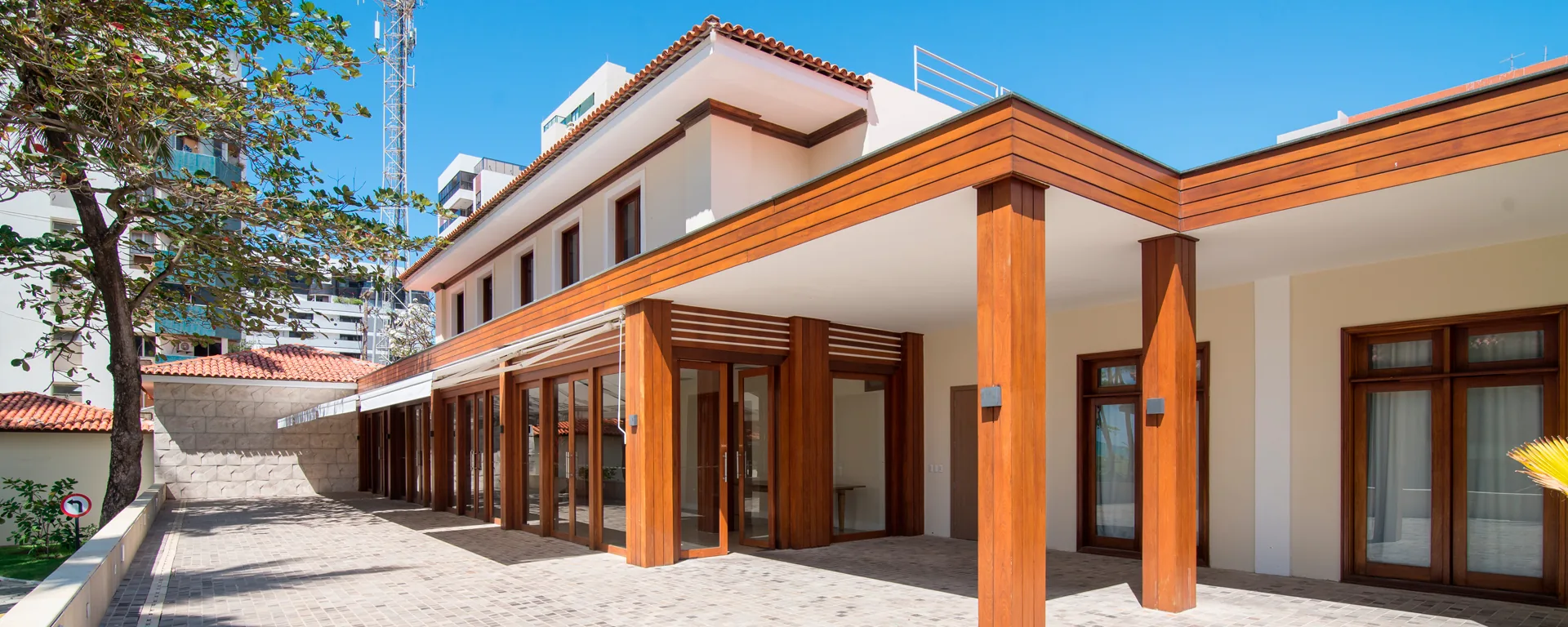 Fachada del centro de eventos del Hotel Jatiúca, con pérgola de madera, puertas de vidrio en cinta y patio pavimentado