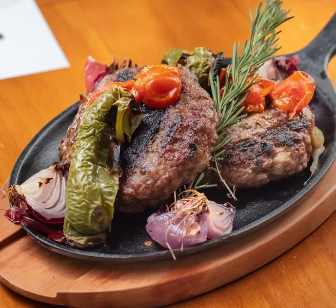 Carne grelhada com pimentão, cebola roxa e alecrim, na chapa de ferro do ¡Vení! Parrilla
