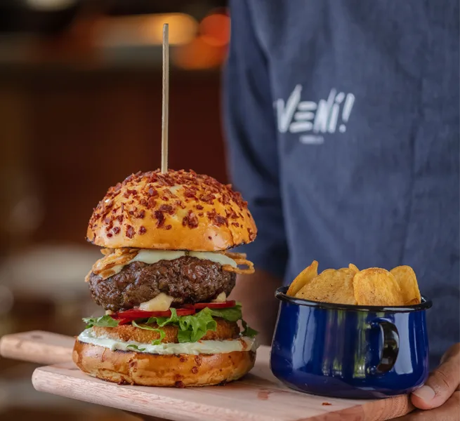 Hambúrguer alto com batatas rústicas, servido no ¡Vení! Parrilla