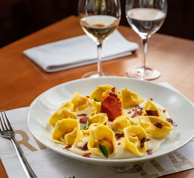 Tortellini com tomate seco e lascas de queijo, servido com vinho branco no ¡Vení! Parrilla