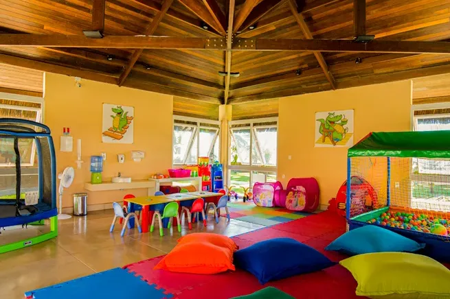 Indoor room at Clubinho do Jacaré, with colourful mats, small tables, a ball pit and the mascot on the panels
