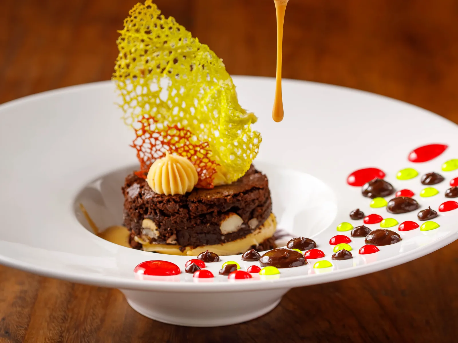 Plated Jatiúca dessert being finished with syrup, tuile and dots of coulis